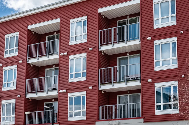 A red four-story apartment building with white-framed windows and a balcony for every unit
