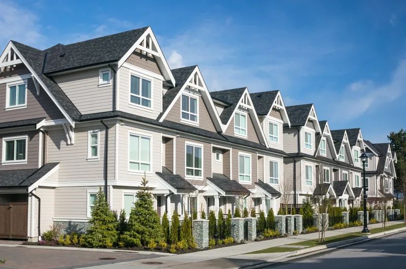 A row of new grey townhomes with peaked roofs and small front gardens along a quiet street