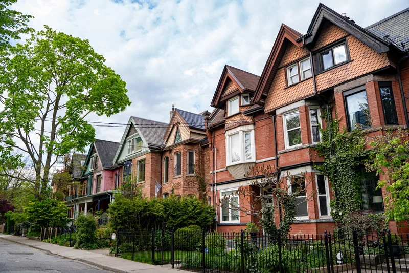 A tree-lined street of red-brick Victorian semi-detached houses with front gardens and iron railings