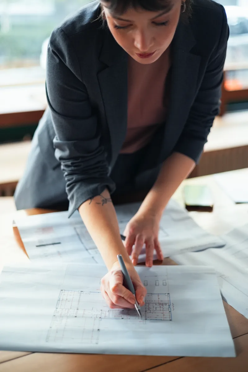 Estimator leaning over a drawing set at a desk, marking quantities with a pencil