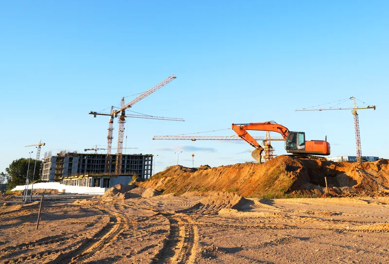 Tower cranes and an excavator working on a large earthwork site on a clear day